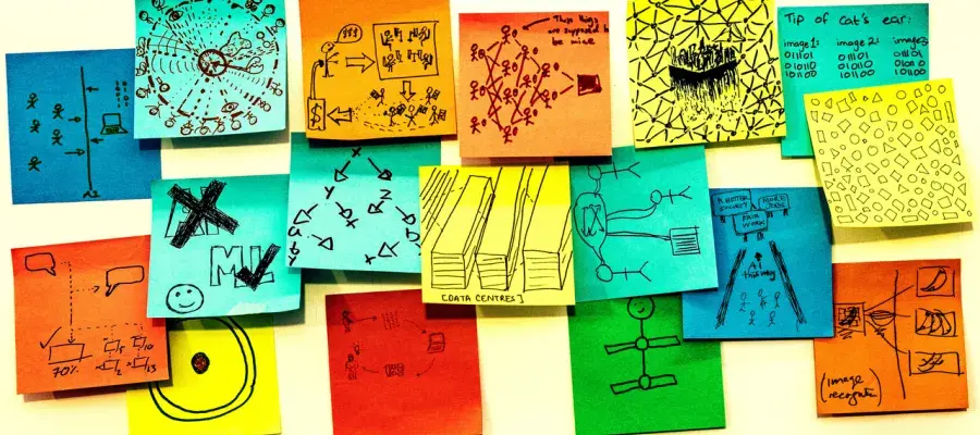 Seventeen multicoloured post-it notes are roughly positioned in a strip shape on a white board. Each one of them has a hand drawn sketch in pen on them, answering the prompt on one of the post-it notes "AI is...." The sketches are all very different, some are patterns representing data, some are cartoons, some show drawings of things like data centres, or stick figure drawings of the people involved.