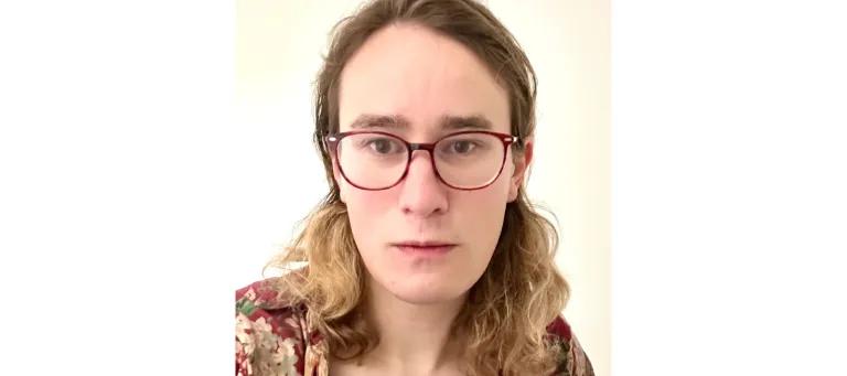 A photo of Esmerela Whittamer, she has long brown hair and is wearing red glasses. 
