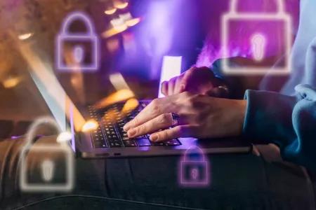 Female hands typing on a laptop in neon light. A lock as a symbol of cybersecurity on a foreground.